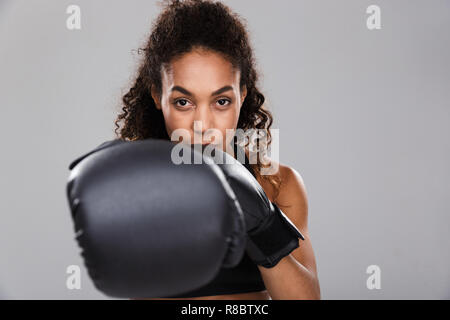 Ritratto di un afro-americano giovane sorridente sportive facendo pugilato isolate su uno sfondo grigio, fotocamera di punzonatura Foto Stock