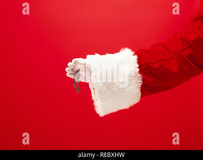 La mano di santa claus tenendo un appartamento o le chiavi dell'auto come dono su sfondo rosso. La stagione invernale, vacanze, celebrazione, concetto di regalo Foto Stock