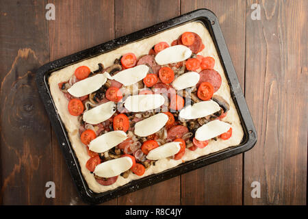 Non cotti pizze con salsiccia per pizza, pomodori, funghi e mozzarella sulla teglia su sfondo di legno Foto Stock