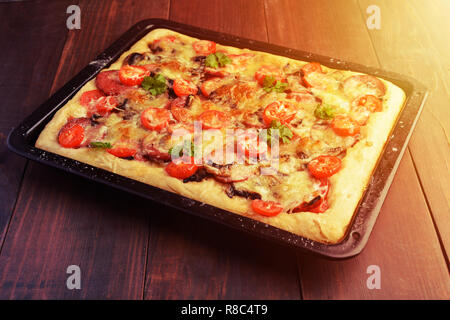 In casa la pizza con pomodori, funghi, salsiccia e verdi su teglia su sfondo di legno, tonica foto Foto Stock