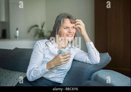 Donna di mezza età in contesti formali ware tenendo una tazza di caffè nel suo appartamento di città Foto Stock