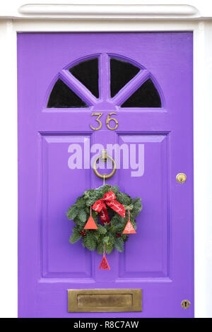 Decorativa ghirlanda di Natale appeso su un colore lilla porta anteriore. Foto Stock