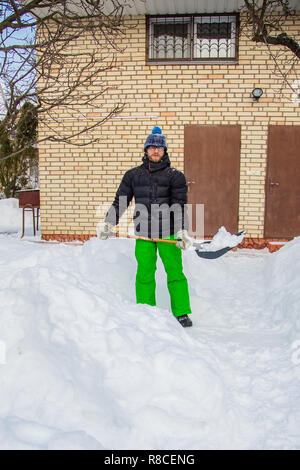 Un uomo che pulisce il cantiere vicino alla sua casa e nel giardino di neve, una soleggiata giornata invernale. Foto Stock