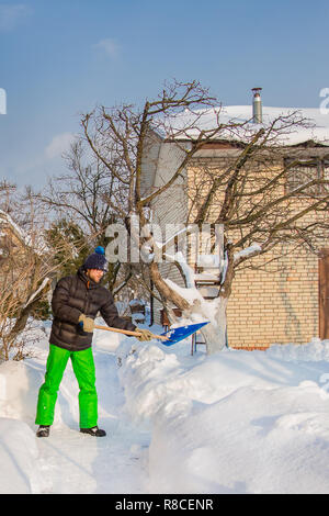 Un uomo che pulisce il cantiere vicino alla sua casa e nel giardino di neve, una soleggiata giornata invernale. Foto Stock