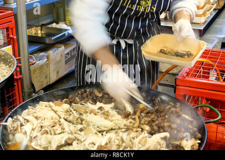 Un cuoco italiano con un grembiule e guanti caldi di cottura di funghi selvatici risotto di farro in un mercato di Borough stallo nella parte sud di Londra Inghilterra REGNO UNITO KATHY DEWITT Foto Stock