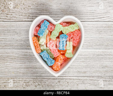 Varietà di diverso colore dolce e aspro di caramelle di zucchero o cibo spazzatura in un cuore ciotola sagomata. Foto Stock