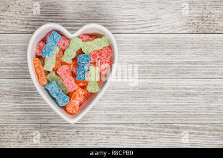 Varietà di diverso colore dolce e aspro di caramelle di zucchero o cibo spazzatura in un cuore ciotola sagomata. Foto Stock