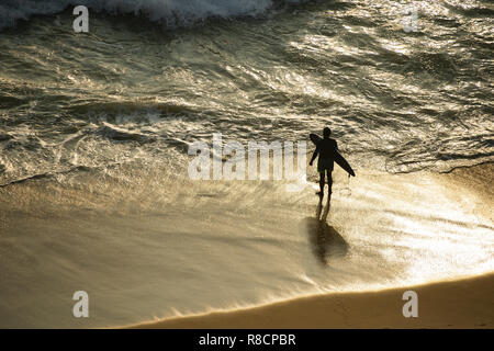 Un turista con la sua tavola da surf è sulla spiaggia di Varkala al tramonto pronti a entrare nel mare. India. Foto Stock