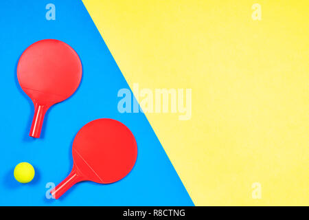 Red racchette da tennis con palla sul blu e sfondo giallo. Foto Stock