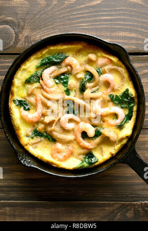 La frittata, funghi e spinaci frittata con gamberetti in padella su un tavolo di legno. Vista superiore, laici piatta Foto Stock