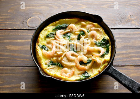 Close up di funghi e spinaci frittata con gamberetti in padella su un tavolo di legno. Foto Stock