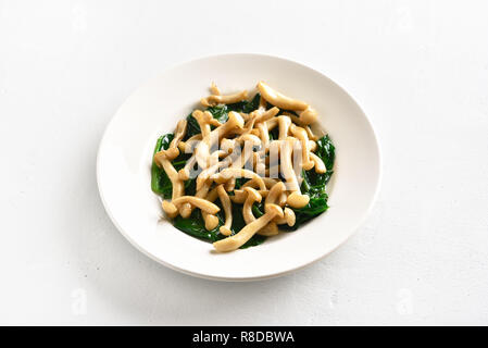 Stir-fried bianco di funghi di faggio con le foglie di spinaci su bianco tavolo di pietra Foto Stock