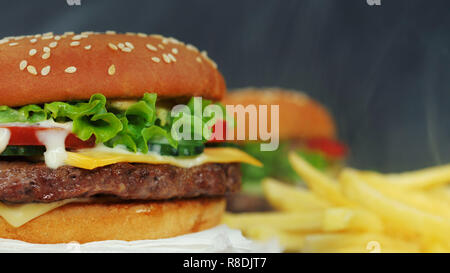 Big appetitosi hamburger con fettine di carne, verdure, formaggi, lattuga e salsa. Hamburger ruota su altro pasto sfondo, vista da vicino. Malsana yu Foto Stock