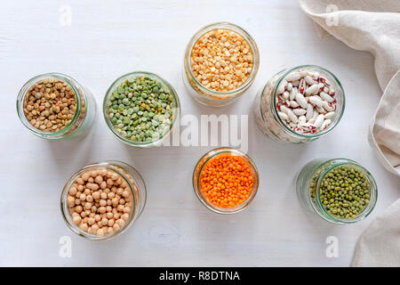 Un assortimento di legumi secchi e legumi in vetro vasi da cucina vista dal di sopra con piselli, lenticchie, fagioli, ceci, su un panno bianco Foto Stock