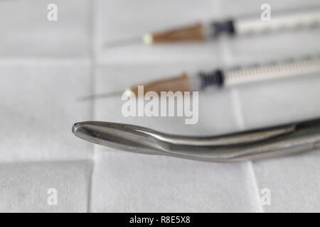 Tampone sterile, pinze e una siringa medica su una tabella dell'ospedale. Accessori nell'ufficio del medico. Sfondo chiaro. Foto Stock