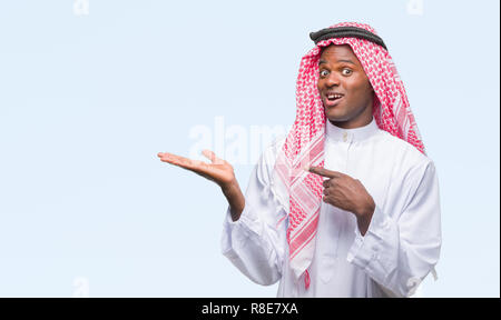 Giovani arabi africano indossando il tradizionale keffiyeh su sfondo isolato stupiti e sorridente alla fotocamera durante la presentazione con la mano e pointin Foto Stock