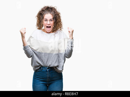 Bella bruna capelli ricci giovane ragazza con gli occhiali su sfondo isolato celebrando sorpreso e meravigliato per il successo con le braccia sollevate e op Foto Stock