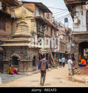 Giovane uomo oltrepassando il piccolo tempio e strada di città in Patan, Lalitpur, Nepal. Foto Stock