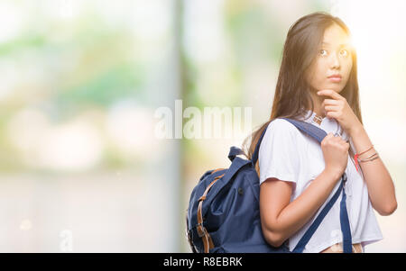 Giovane donna asiatica che indossa uno zaino e cuffie isolato su sfondo faccia seriamente pensando di domanda, molto confusa idea Foto Stock