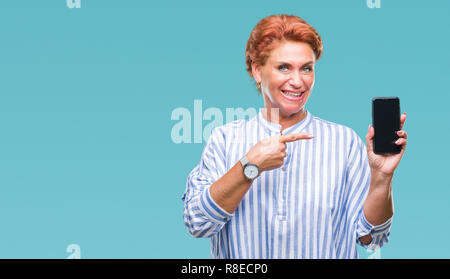 Accattivante senior redhead caucasica donna che mostra lo schermo dello smartphone su sfondo isolato molto felice puntando con mani e dita Foto Stock