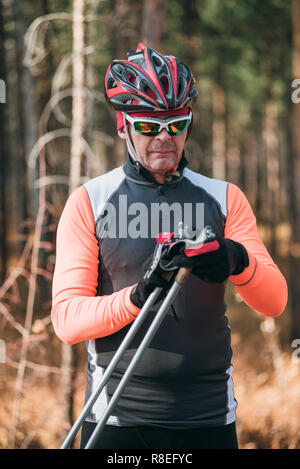 La formazione di un atleta sul rullo pattinatori. Il biathlon ride sul rullo di sci con bastoncini da sci, nel casco. Allenamento di autunno. Sport a rullo. Uomo adulto rid Foto Stock