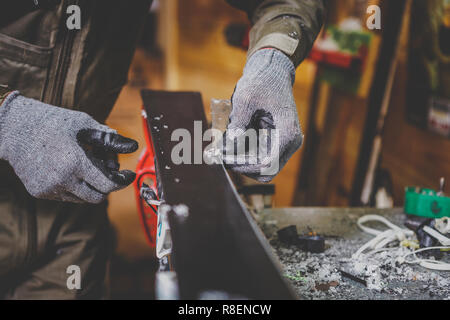 Un lavoratore di sesso maschile in un servizio sci riparazioni in officina la superficie di scorrimento dello sci. Close-up di una mano con una lottatrice di plastica per la rimozione di cera, rimozione Foto Stock