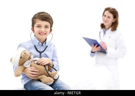 Ragazzo giochi di ruolo con Teddy bear e stetoscopio con medico in background. Foto Stock