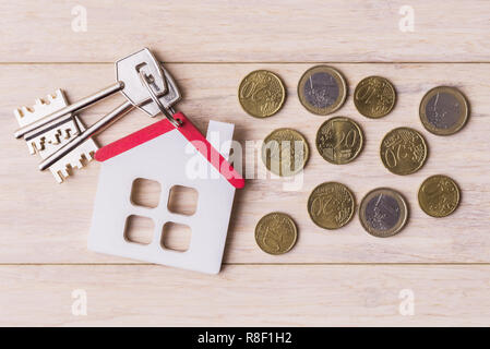 Modello di casa con chiavi e monete in euro al di sopra della luce di sfondo di legno Foto Stock