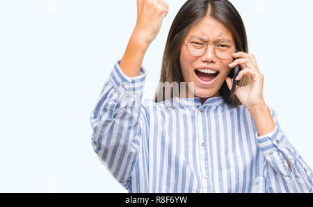 Giovane donna asiatica parlando al telefono su sfondo isolato infastiditi e frustrato grida con rabbia, crazy e urla con la mano alzata, rabbia Foto Stock