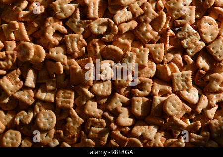 Un sacco di piccoli giallo cracker salati in forma stampata di lettere inglesi, i quali giacciono su di un tagliere di legno di close-up. Immagine di sfondo di salato Foto Stock