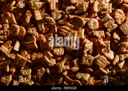 Un sacco di piccoli giallo cracker salati in forma stampata di lettere inglesi, i quali giacciono su di un tagliere di legno di close-up. Immagine di sfondo di salato Foto Stock