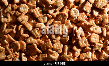 Un sacco di piccoli giallo cracker salati in forma stampata di lettere inglesi, i quali giacciono su di un tagliere di legno di close-up. Immagine di sfondo di salato Foto Stock