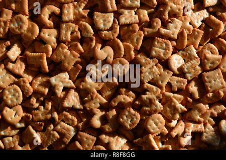 Un sacco di piccoli giallo cracker salati in forma stampata di lettere inglesi, i quali giacciono su di un tagliere di legno di close-up. Immagine di sfondo di salato Foto Stock