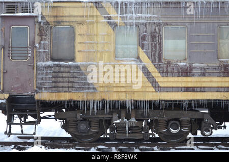 Foto dettagliate di una vettura congelate di treni passeggeri con ghiaccioli e ghiaccio sulla sua superficie. Stazione ferroviaria nella fredda stagione invernale Foto Stock