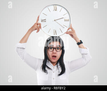 Foto immagine ritratto di una giovane e bella Asian imprenditrice sembrava sconvolto mentre cercano ora sul clock, con entrambe le mani tenendo il clock, mezzo corpo Foto Stock