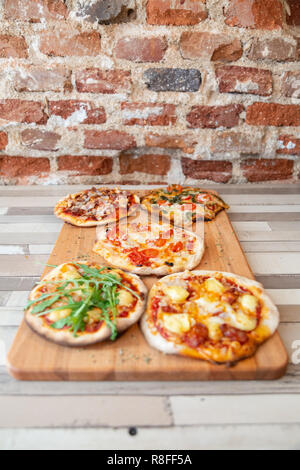 Cinque pizzette su una tavola di legno su un tavolo in legno e un muro di mattoni Foto Stock