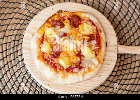 Salsiccia per pizza pizza su un cerchio di legno su una tovaglia di rafia su un tavolo di legno. Foto Stock