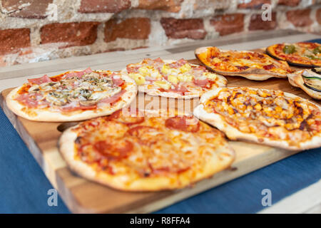 Sette piccole pizze su una tavola di legno, freschi di forno, pronto a mangiare in un ristorante. Il focus è sulla carbonara e quelli di Hawaiian. Su un woode Foto Stock