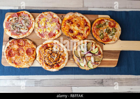 Vista aerea di sette piccole pizze su una tavola di legno, freschi di forno, pronto a mangiare in un ristorante. Su un tavolo di legno con una tovaglia blu e Foto Stock