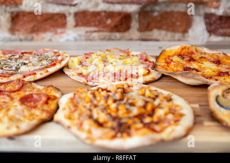 Sei piccole pizze su una tavola di legno, freschi di forno, pronto a mangiare in un ristorante. Con focus su hawaiian pizza. Su un tavolo di legno con un blu t Foto Stock