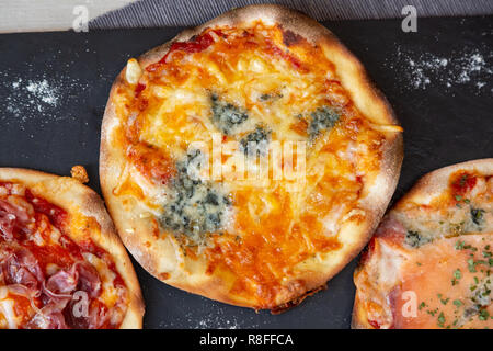 Vista aerea di una quattro formaggi pizza su una lavagna nera guarnire con farina e una tovaglia di colore grigio Foto Stock