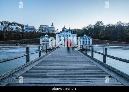 Vista da un pontile sulla spiaggia di una città. Ponte di atterraggio è in legno con un edificio. In fondo è una città. Nel mezzo. Foto Stock