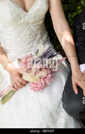 Sposa e lo sposo tenendo le mani su un parco con il bouquet e gli anelli di nozze Foto Stock