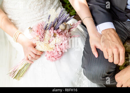 Sposa e lo sposo tenendo le mani su un parco con il bouquet e gli anelli di nozze Foto Stock