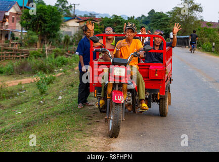 Thakhek, Laos - Aprile 20, 2018: bevuto paesani dicendo ciao da un carrello mentre il conducente è fumare in una remota zona rurale del Laos Foto Stock