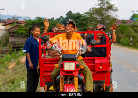 Thakhek, Laos - Aprile 20, 2018: bevuto paesani dicendo ciao da un carrello mentre il conducente è fumare in una remota zona rurale del Laos Foto Stock