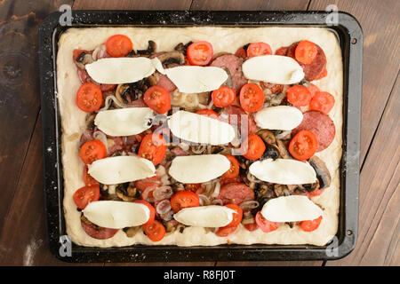 (Nella quasi totalità) impreparati pizza fatta in casa con ingredienti sulla teglia marrone su sfondo di legno Foto Stock