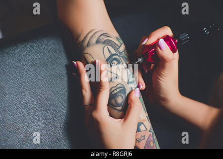 Ragazza tattoo artist facendo un tatuaggio sulla sua mano, rosa macchina da scrivere su una tavola nera. Foto Stock