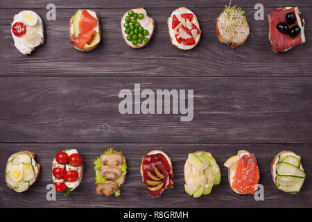 Crostini vari preparati con diversi ripieni di salmone, cetriolo, pomodoro ciliegino, mozzarella, uova, funghi, olive, avocado, mandorle. Foto Stock