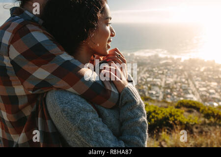 Giovane rilassante in vacanza. Bella giovane donna essendo abbracciando con il suo fidanzato da dietro, con entrambi i piedi sulla scogliera e guardando a vista. Foto Stock